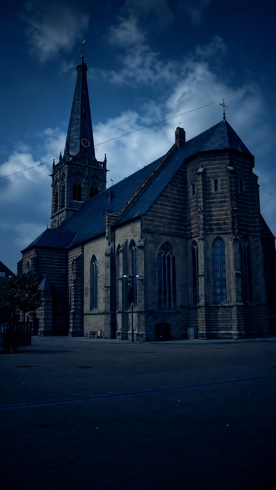 Een impressie van de Catharinakerk in Doetinchem vanaf het Simonsplein: de toren en het veelhoekige koor onder een donkerblauwe lucht.