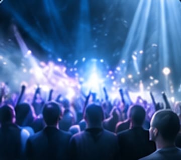 A crowd with arms raised under violet and blue light.